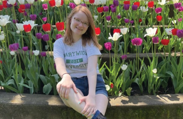 Young woman sitting down in front of flowers smiling wearing a marywood university shirt.